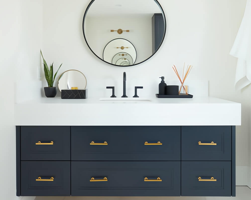 Floating navy blue bathroom vanity with white engineered stone countertop matte black faucets gold hardware black round mirror and gold-and-glass wall sconces