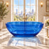 Front view of a 64-inch transparent blue resin freestanding bathtub beside a large window in a marble bathroom.