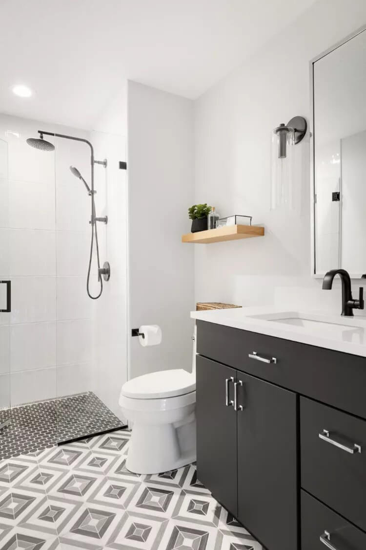Black vanity cabinets, paired with silver hardware and a bold geometric tile pattern in shades of gray, black, and white