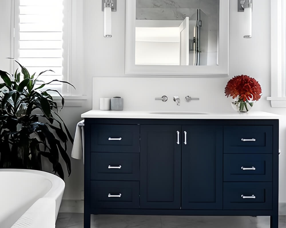 Navy blue bathroom vanity with white stone countertop, marble tile floor, silver handles, white-framed mirrors, vertical wall lights, green plants, and red flowers